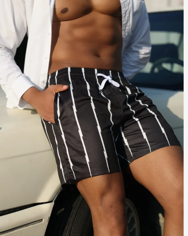 Man in wholesale black stripe mesh shorts with open white shirt leaning against vintage car